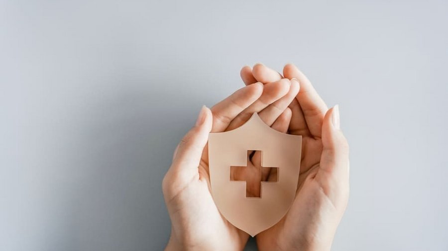 Mâini care țin un scut cu simbolul crucii, asigurare de sănătate, prim ajutor, asistență medicală și concept de bunăstare. 
