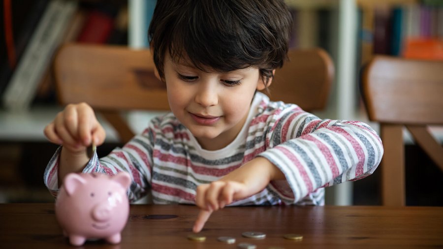 Copil cu o pușculiță în formă de porc și monede - costuri fixe lunare în gospodărie