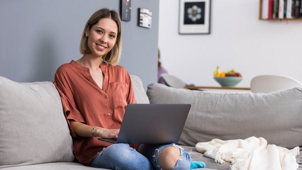 Femeie care lucrează acasă cu un laptop pe canapea
