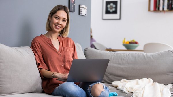 Femeie care lucrează acasă cu un laptop pe canapea Femeie care lucrează acasă cu un laptop pe canapea
